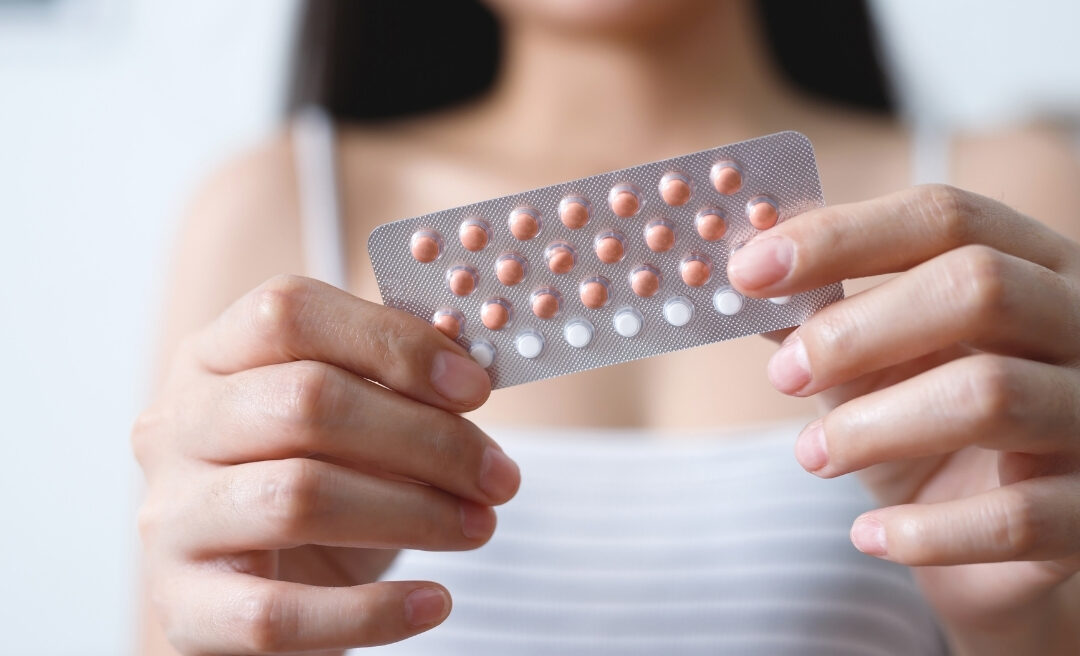 Close-up of a person holding a blister pack of contraceptive pills, part of a detailed women’s health guide at Hodgson Pharmacy.